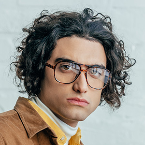 The Grant Getters A person with curly hair and glasses wearing a white turtleneck and brown jacket, representing The Grant Getters, looks directly at the camera against a light background. Grant Writing